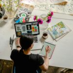 Artistic workspace featuring calligraphy and digital design on a tablet and laptop.